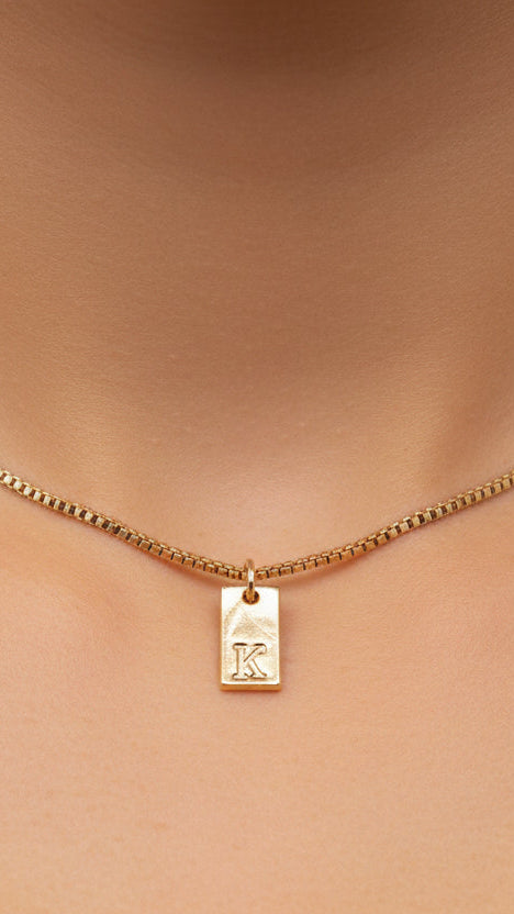 Gold, necklace with a pendant on a person's neck against a neutral background