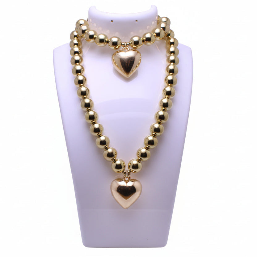 Gold beaded necklace with heart pendants on a white mannequin bust.