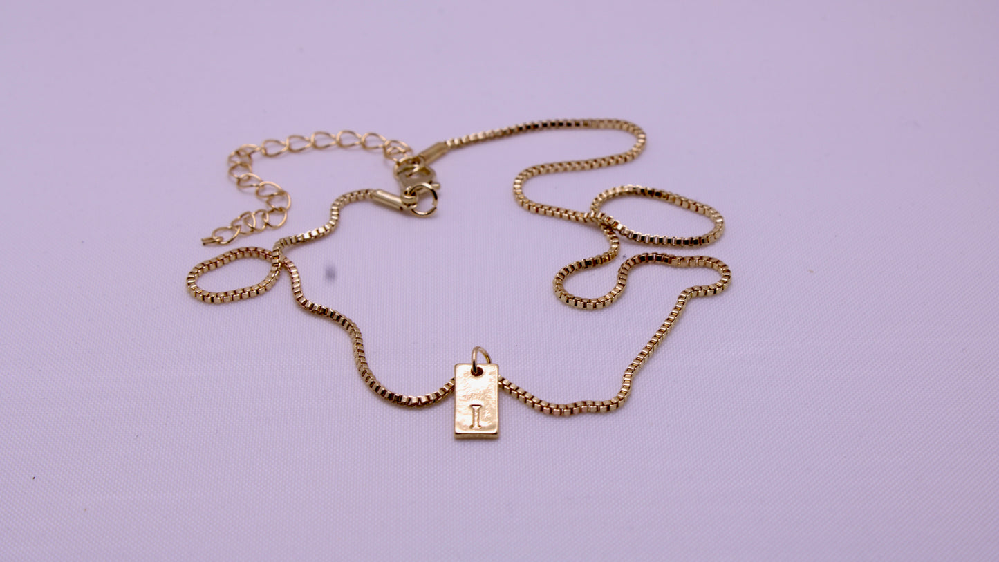 Gold chain necklace with a tag on a light purple background